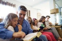 father in Portugal sits with his children in their living room to read from the scriptures together
